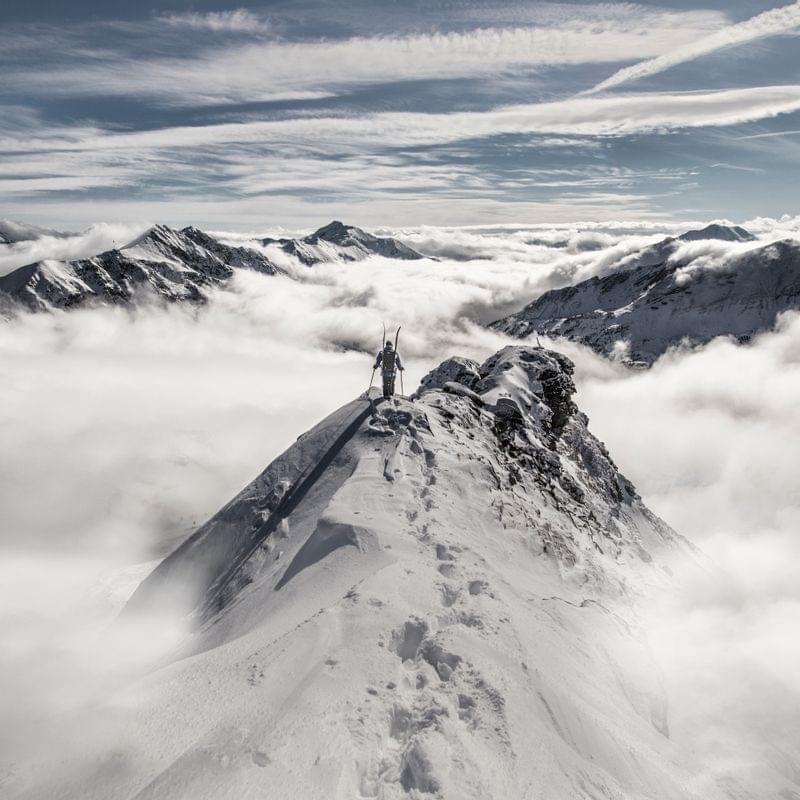 Skifahrer auf verschneitem Bergrücken über den Wolken in den Alpen
